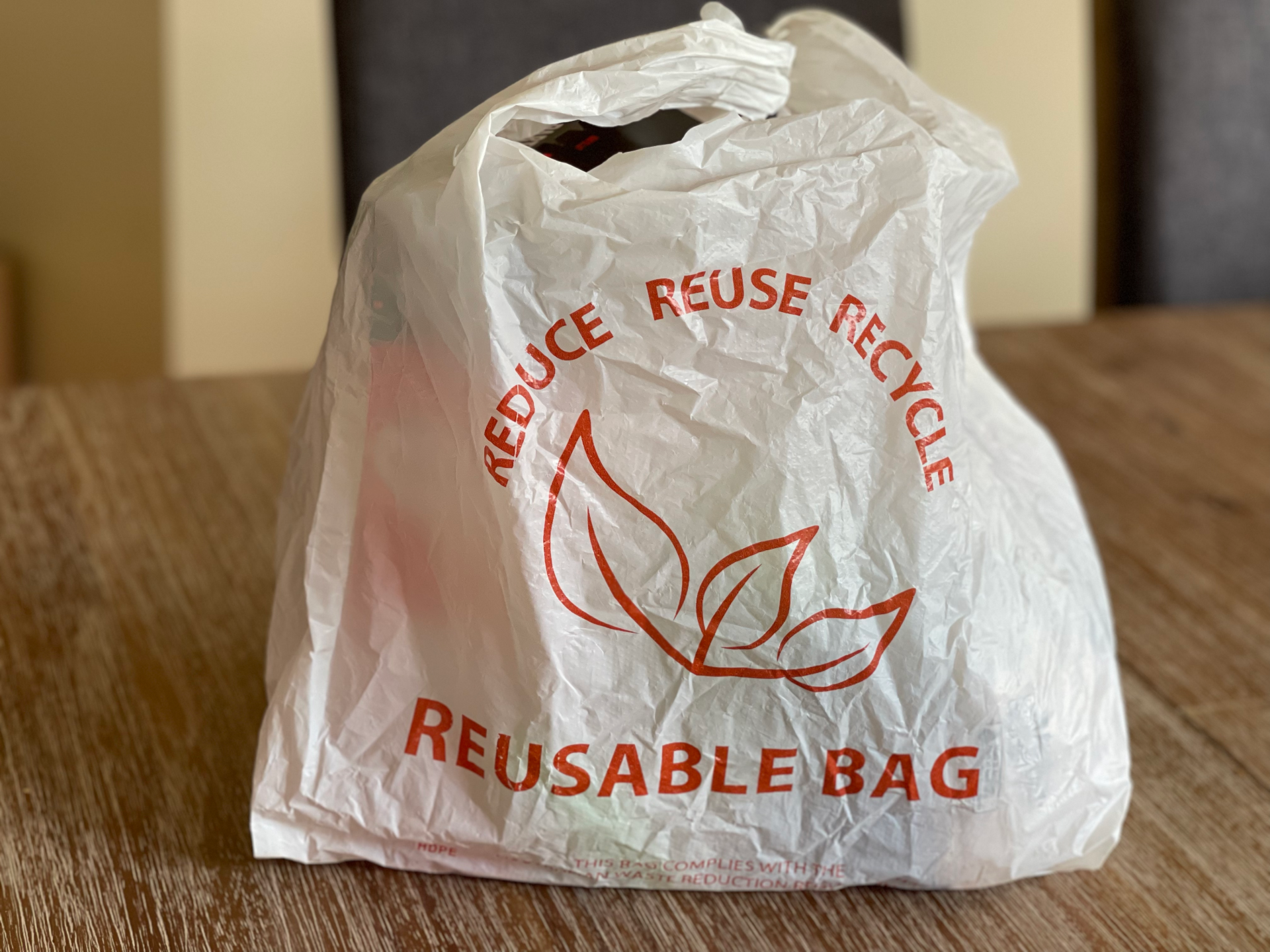 Reusable bag promoting reduce, reuse, recycle on a wooden table indoors.